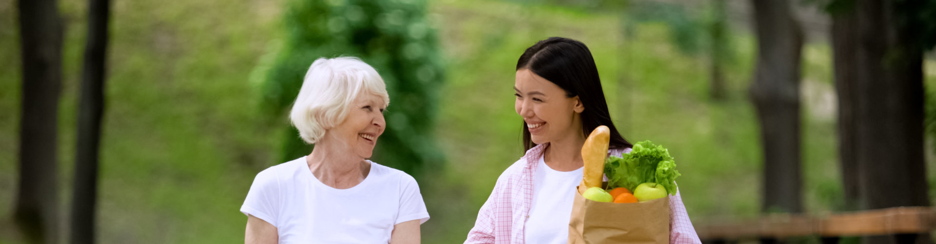 Elderly patient and nurse walking while nurse carries grocery